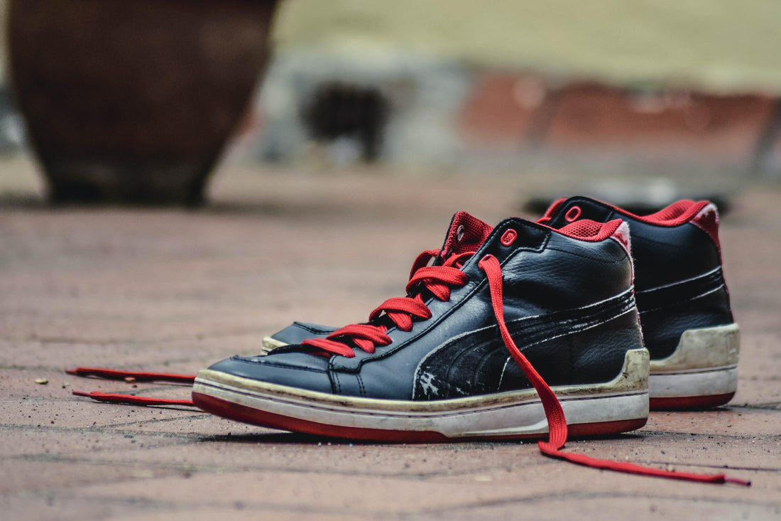 Black high top sneakers with untied red shoelaces.